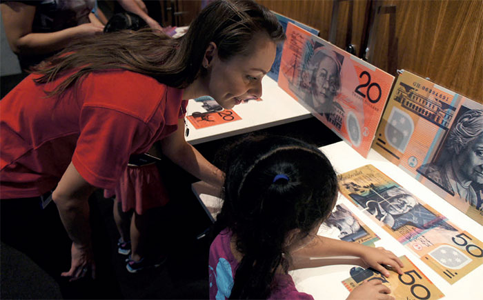(Image top) Visitors to the Reserve Bank of Australia Museum on Australia Day, January 2016; (image above) Note Issue Department's Kristin Langwasser assists a young visitor with a banknote puzzle, January 2016